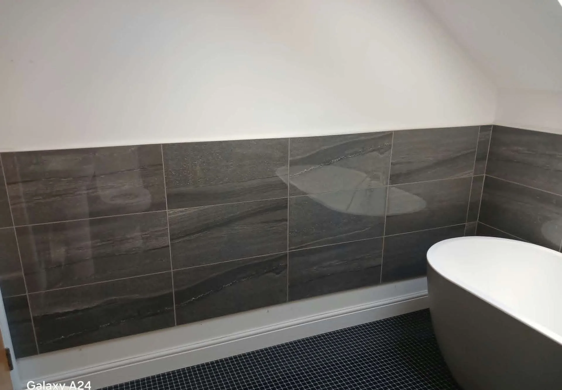 Large-format slate-effect wall tiles with fine grout above a freestanding bath