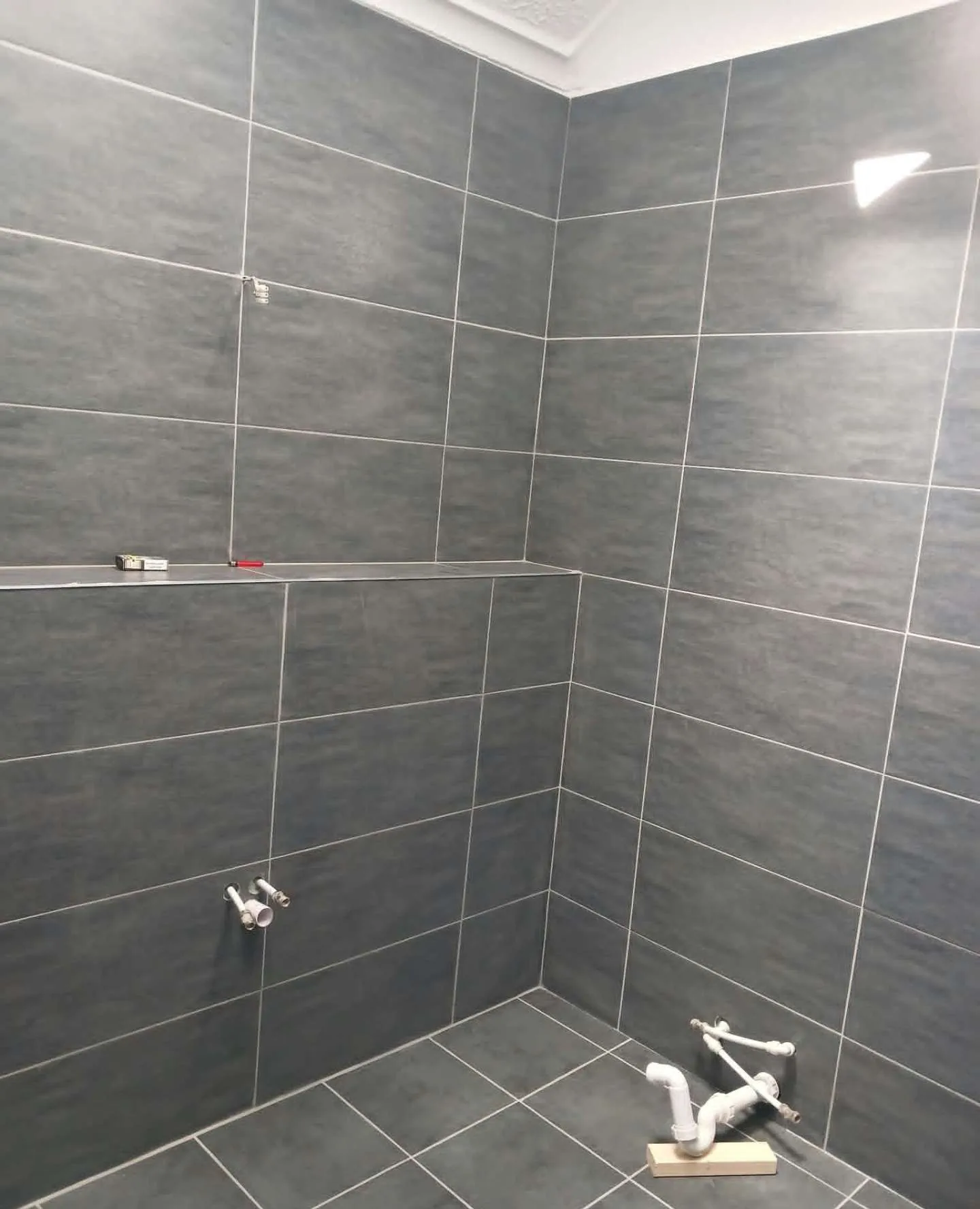 Dark grey wall and floor tiles with a built-in tiled ledge, ready for sanitaryware